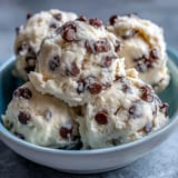 A creamy scoop of Greek Yogurt Cookie Dough shows rich chocolate chips and a smooth texture on a rustic marble countertop.