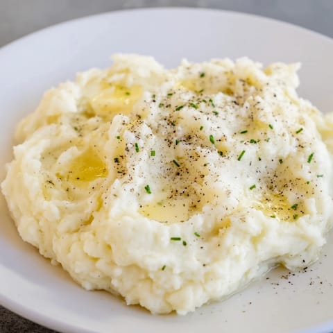 Golden Mashed Potatoes being mashed with a potato masher, showing a smooth, buttery texture and steam rising.