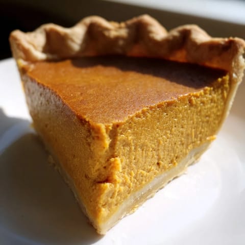 Freshly baked Pumpkin Pie with a golden, flaky crust and a perfectly set, spiced custard filling on a rustic plate.