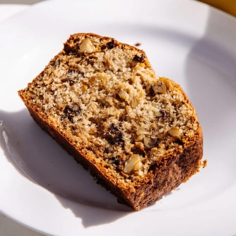 A rustic loaf of Banana Bread topped with chopped walnuts, served on a wooden board for breakfast.