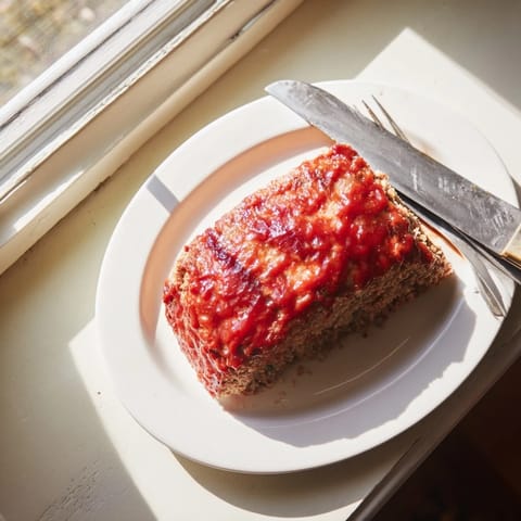 Savory Classic Meatloaf slice reveals tender ground beef and onion interior, paired with creamy mashed potatoes and green beans.