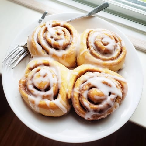 Homemade Cinnamon Rolls featuring fluffy spiraled dough, gooey brown sugar, and cinnamon filling on a rustic wooden table.