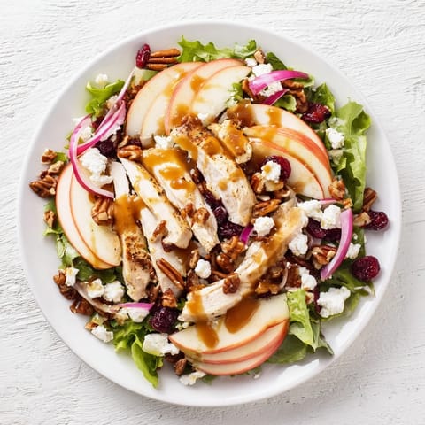 An autumn salad with apple slices, glazed chicken, and candied pecans, finished with a glossy caramel dressing on a rustic platter.  