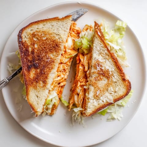 Golden Buffalo Chicken Caesar Grilled Cheese sandwich on a plate, with melted provolone and shredded romaine lettuce.  