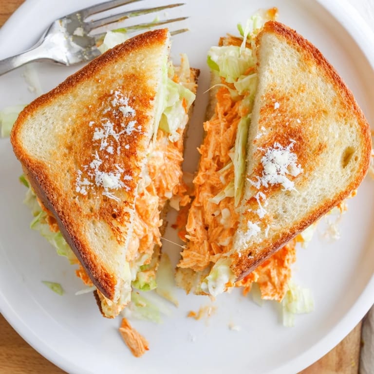 Freshly grilled Buffalo Chicken Caesar Grilled Cheese, drizzled with buffalo sauce and sliced to show layers.  