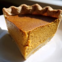Freshly baked Pumpkin Pie with a golden, flaky crust and a perfectly set, spiced custard filling on a rustic plate.