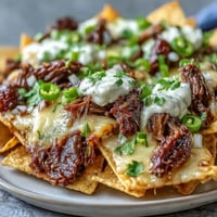 Crispy tortilla chips layered with smoky BBQ beef and melty cheddar cheese, fresh jalapeños and cilantro on top.